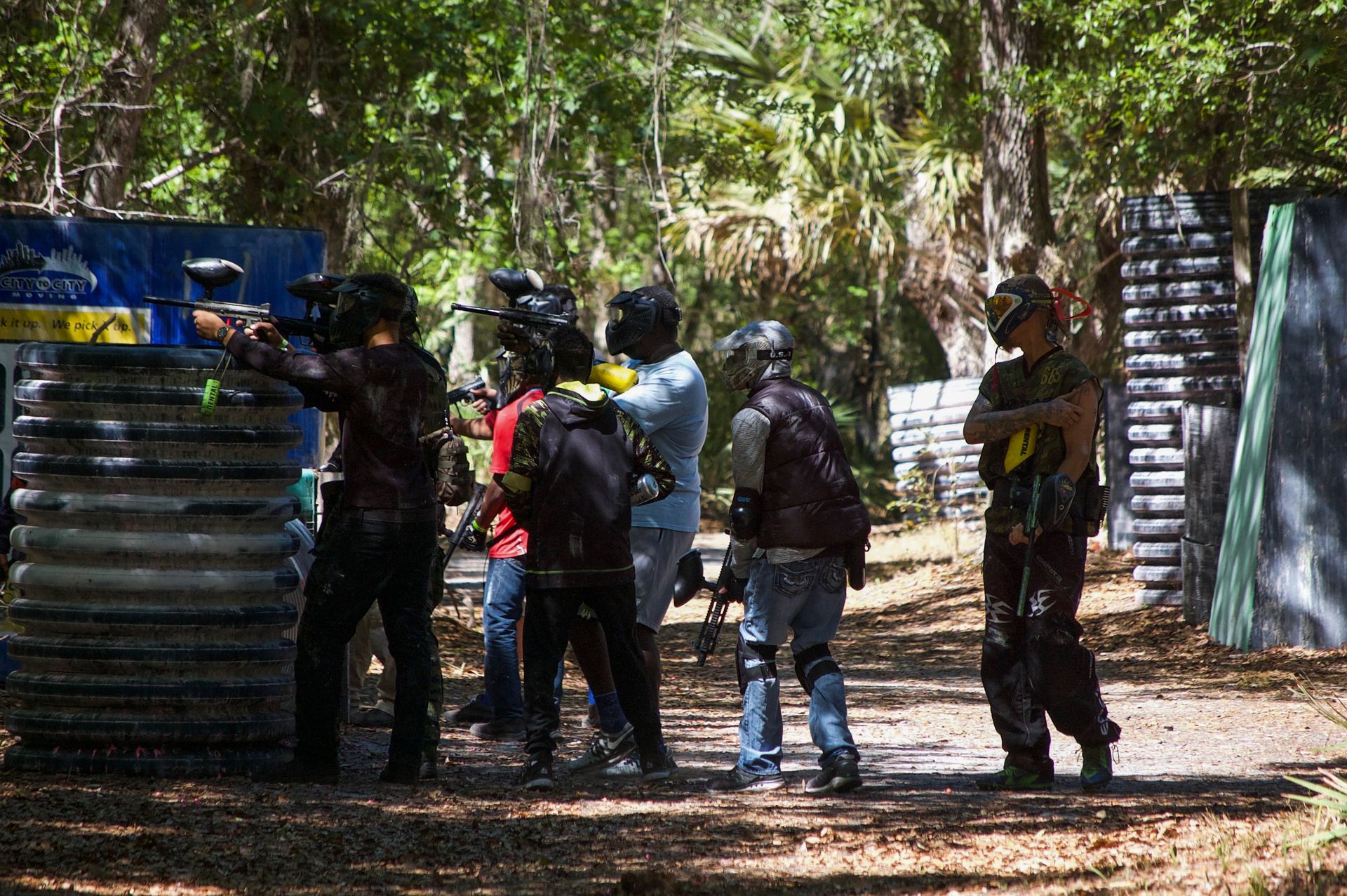 Foster teens and volunteers in masks and gear during a paintball outing, seen from behind