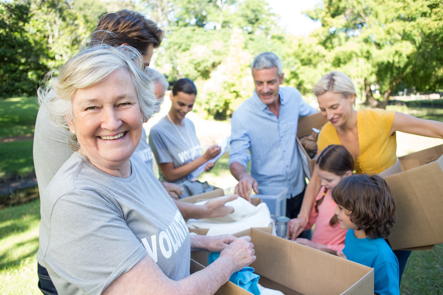 A smiling older volunteer sorting donated clothing with a family of volunteers in a sunny park
