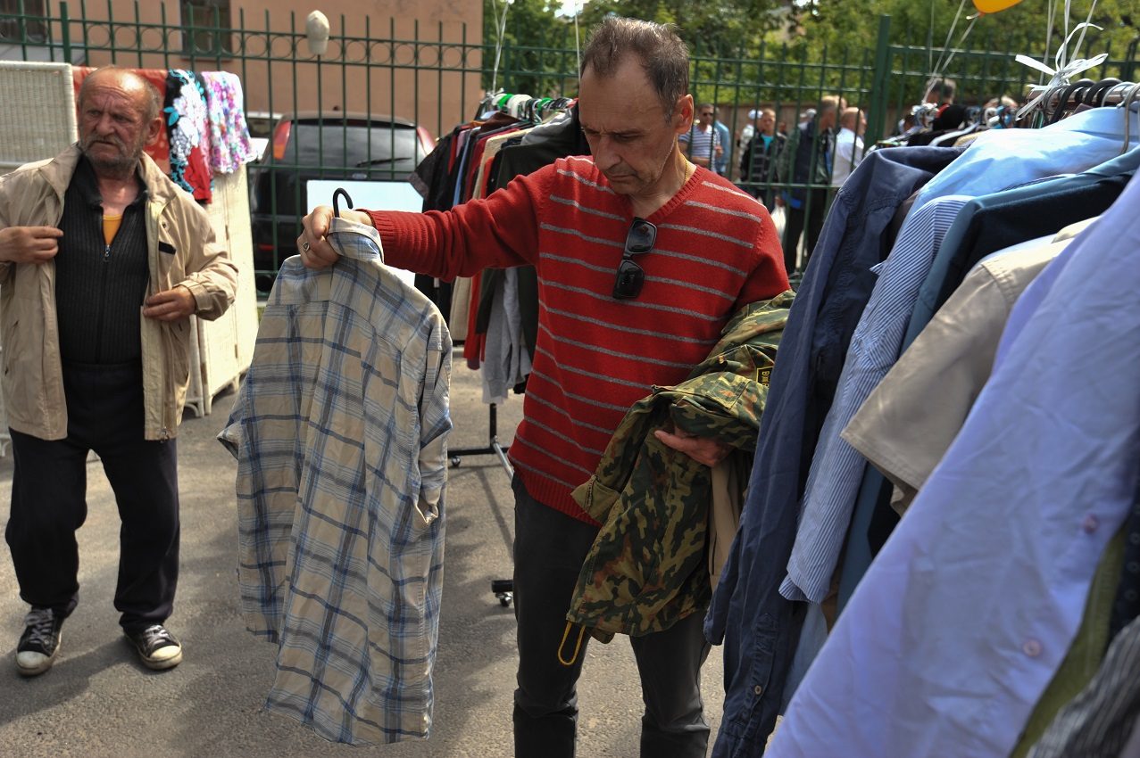 Two men looking through racks of donated clothing at an outdoor free clothing distribution